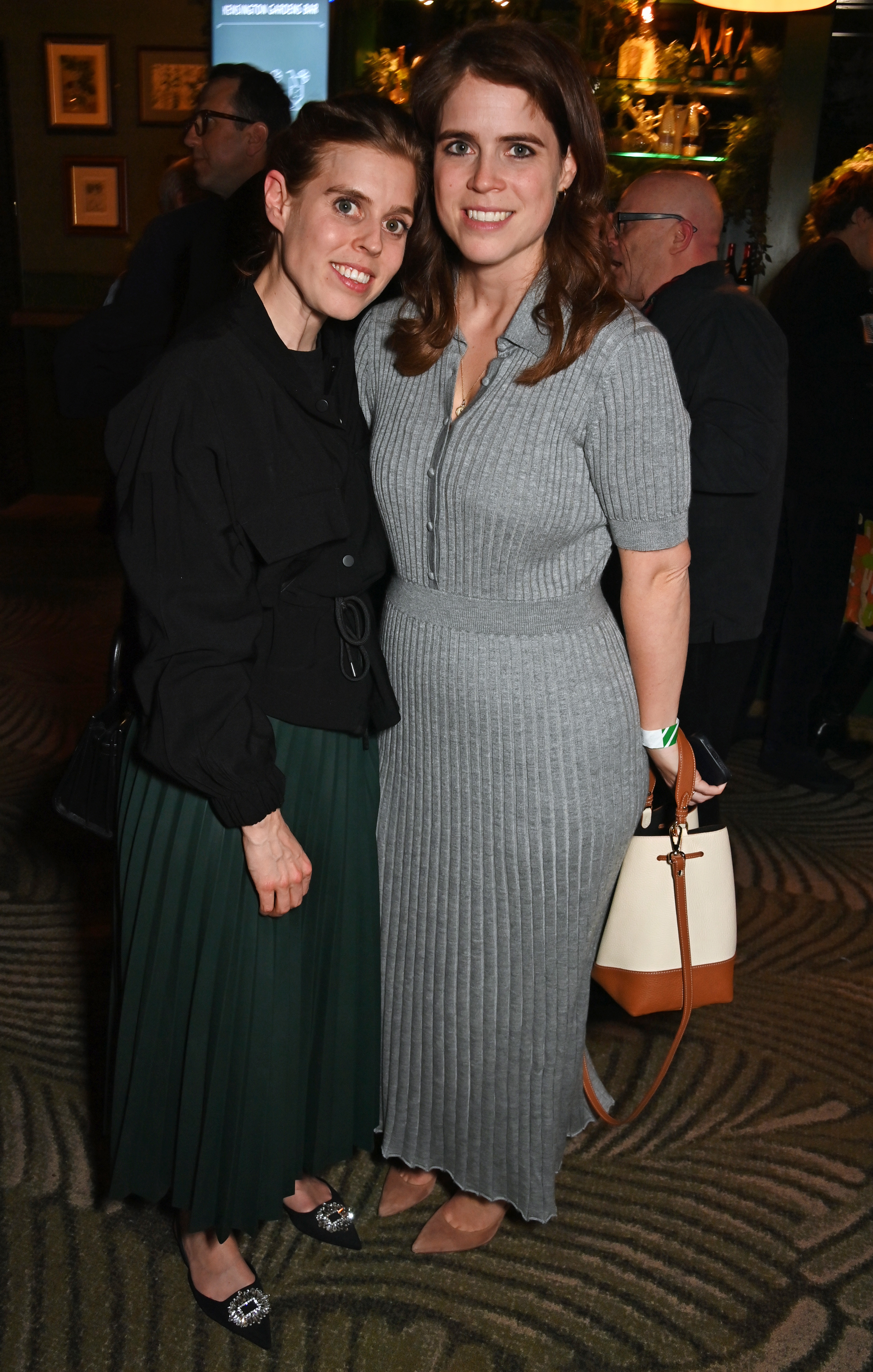 Princess Eugenie and Princess Beatrice wearing long skirts standing next to each other at a party