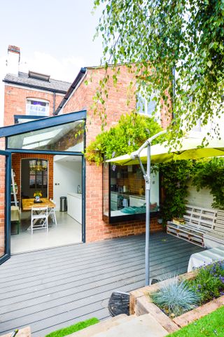 a side return extension with roof windows – a glass extension with a dining table inside, next to a brick house, with a small grey patio out front