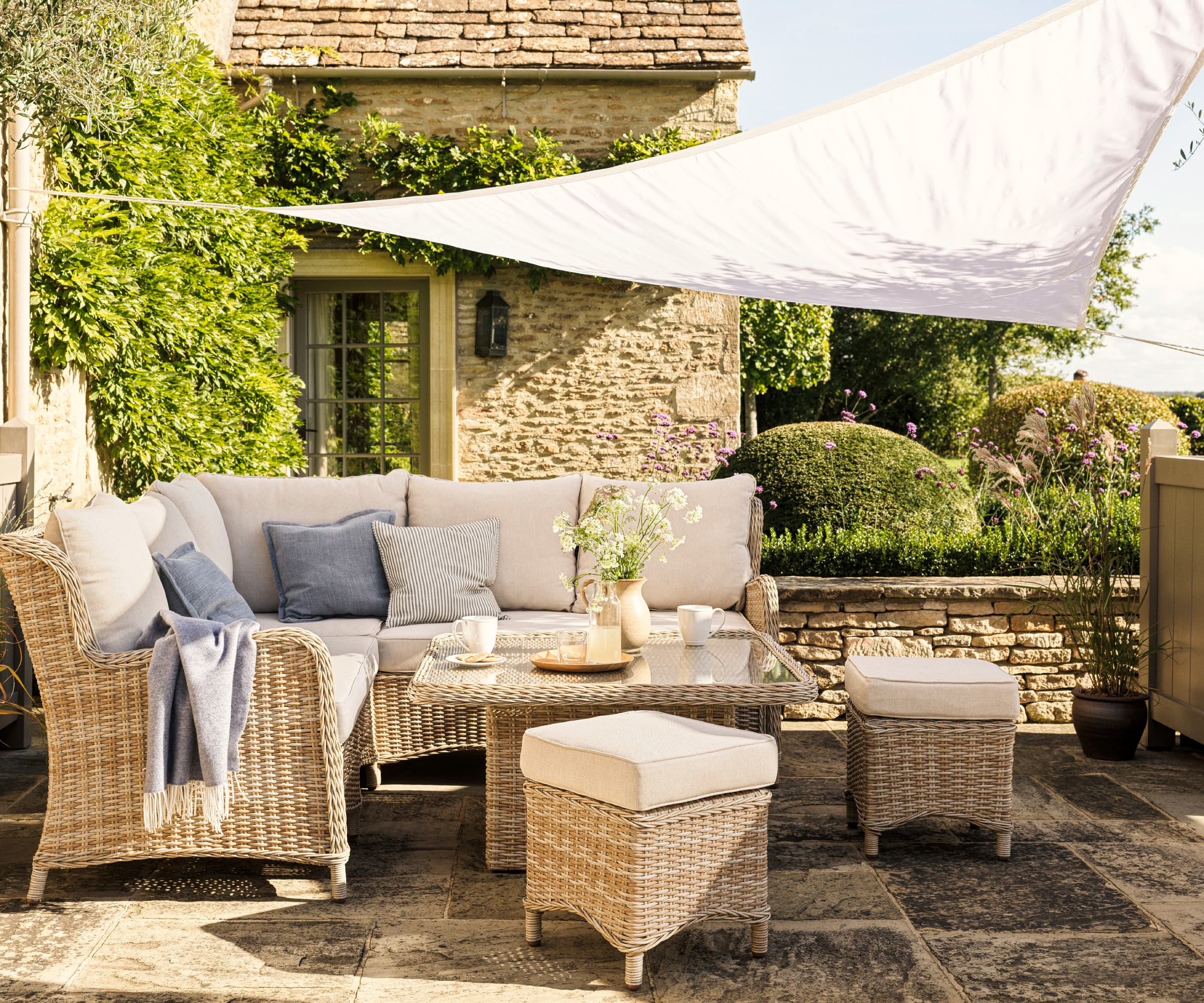 white shade sail over rattan cushioned patio set on cottage garden patio