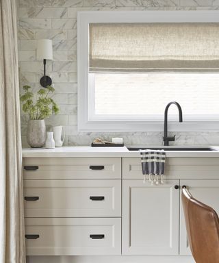 A detail of a kitchen with greige cabinets and marble-tiled walls