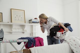 A woman does laundry while talking on the phone.