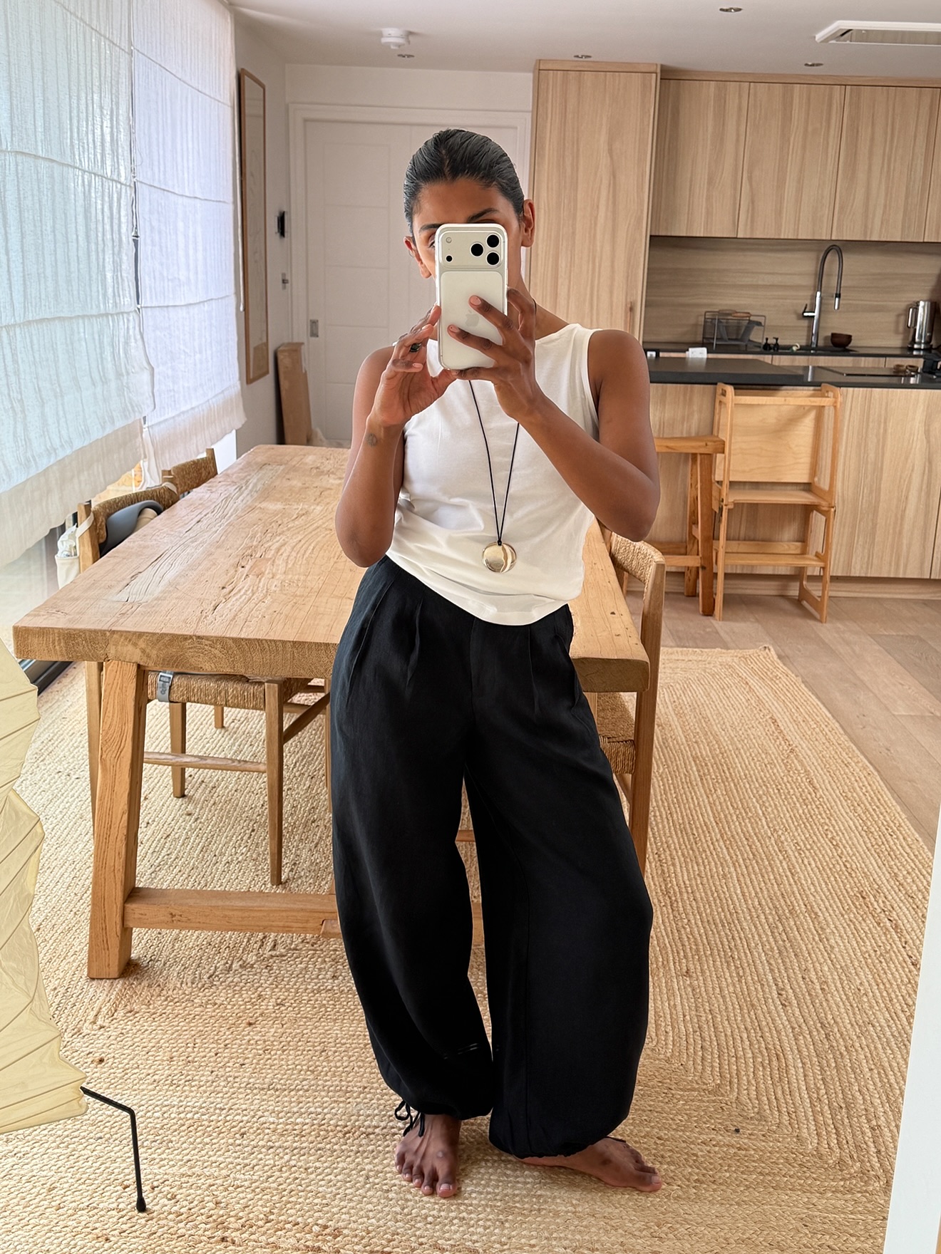 An image of @monikh wearing balloon trousers, one of the best anti-jeans summer trouser trends with a white tank top.