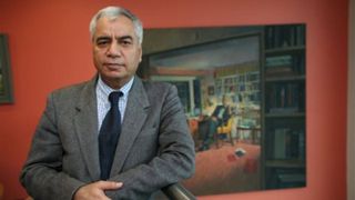 Photo of psychiatrist Dr Dinesh Bhugra wearing a gray suit and navy tie and standing in front of a large painting