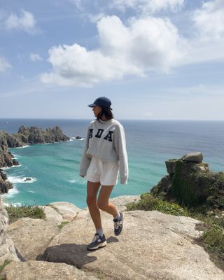 Summer rainy day outfits: @jessicaskye_ wears a sweatshirt with shorts and a baseball cap