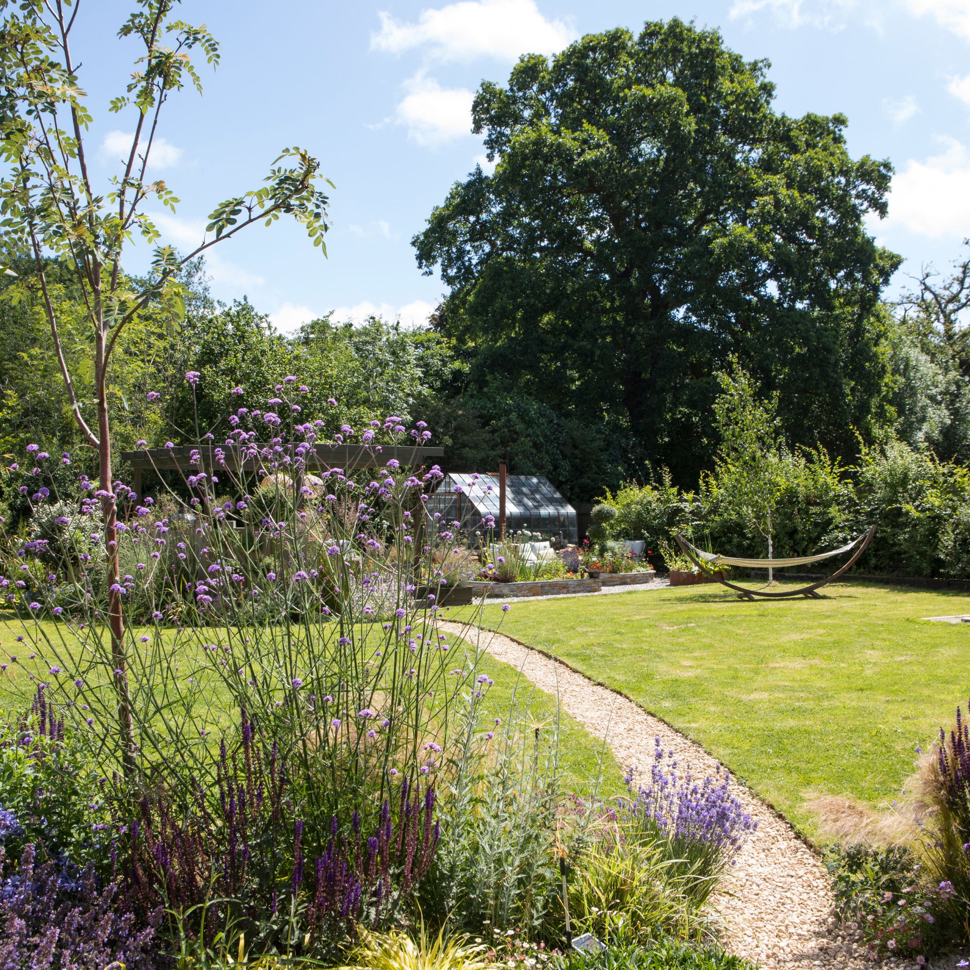 Garden with trees and grass and planted borders, with a gravel pathway through the middle and a hammock on the grass