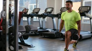 Man performing dumbbell lunge in front of row of treadmills
