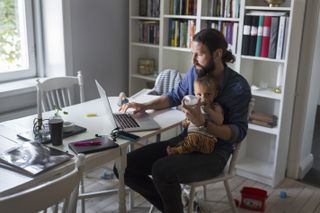 Father feeding baby boy while using laptop at home