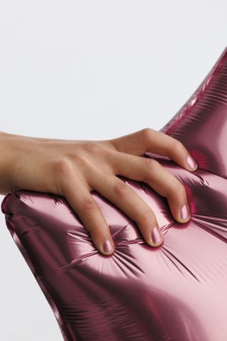 A hand holding a pink balloon wearing Pleasing x JW Anderson pink nail polish