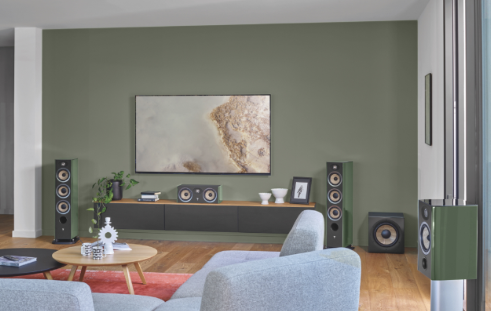 A contemporary living room features a full Focal surround sound system in a muted green finish, including floor-standing and center-channel speakers.