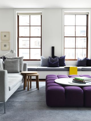 A living room with purple ottoman and grey sofa