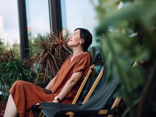 A woman sits peacefully on a chair surrounded by plants