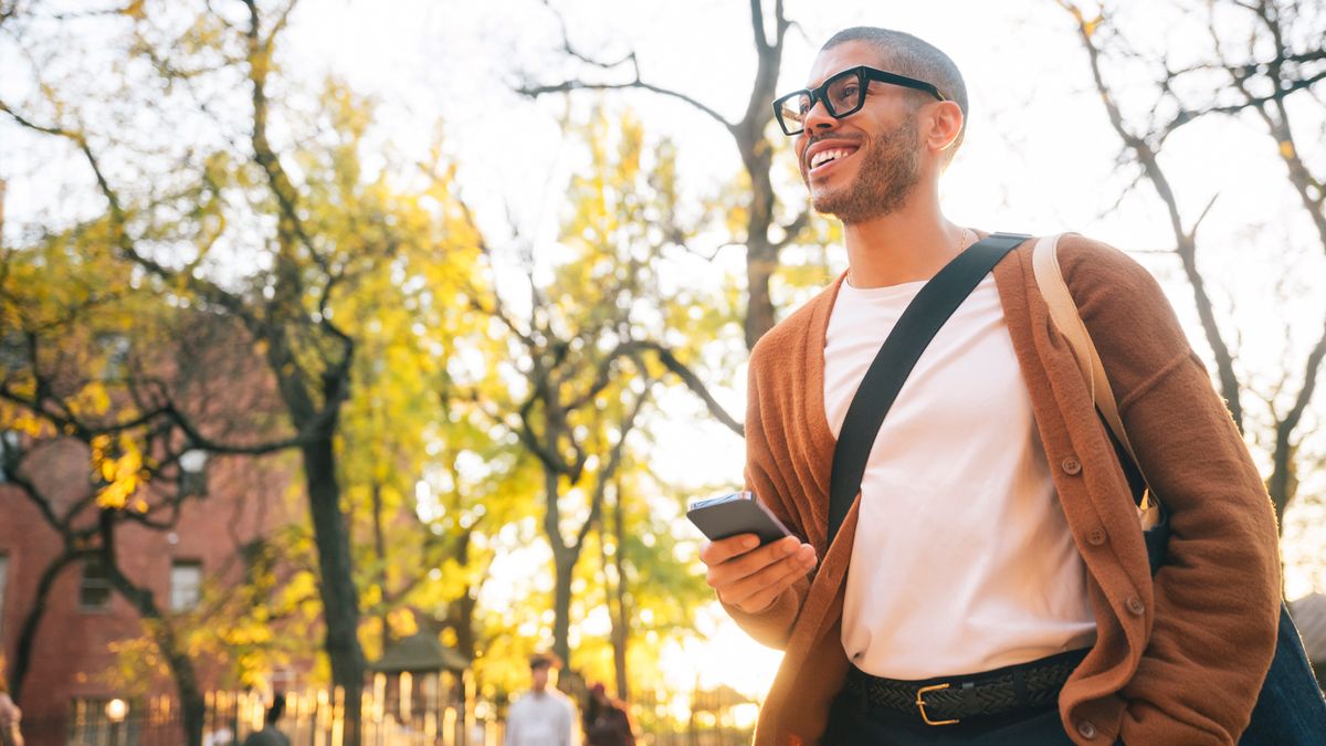 A man stands outside, smiling, with a smartphone in hand