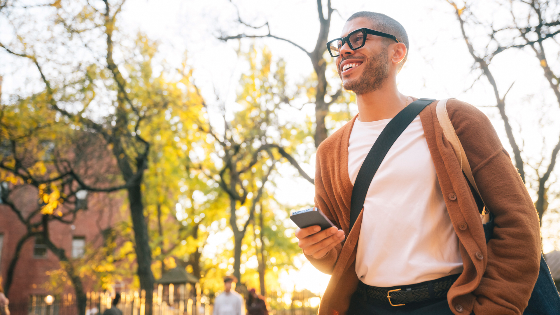 A man stands outside, smiling, with a smartphone in hand