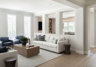 formal living room with white sofas and wooden coffee table and gray leather armchairs and wall cut outs to family room a