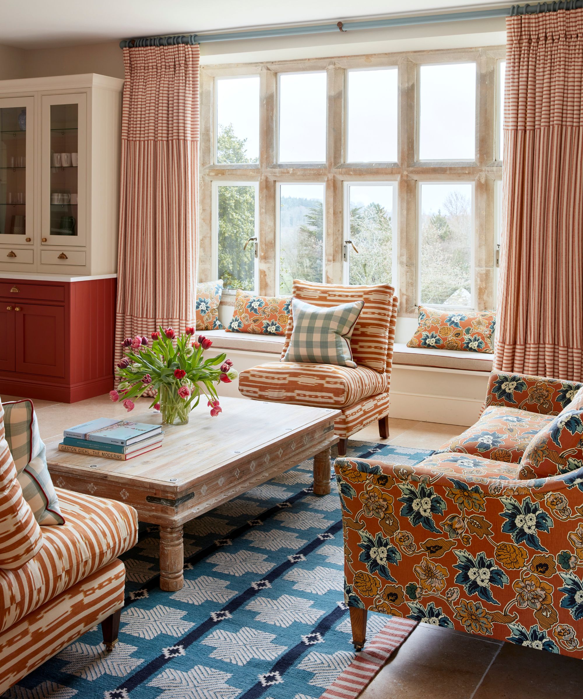 A soft kitchen with a break out lounge area with a blue patterned rug, orange and blue floral sofa, wooden coffee table and two patterned orange slipper chairs