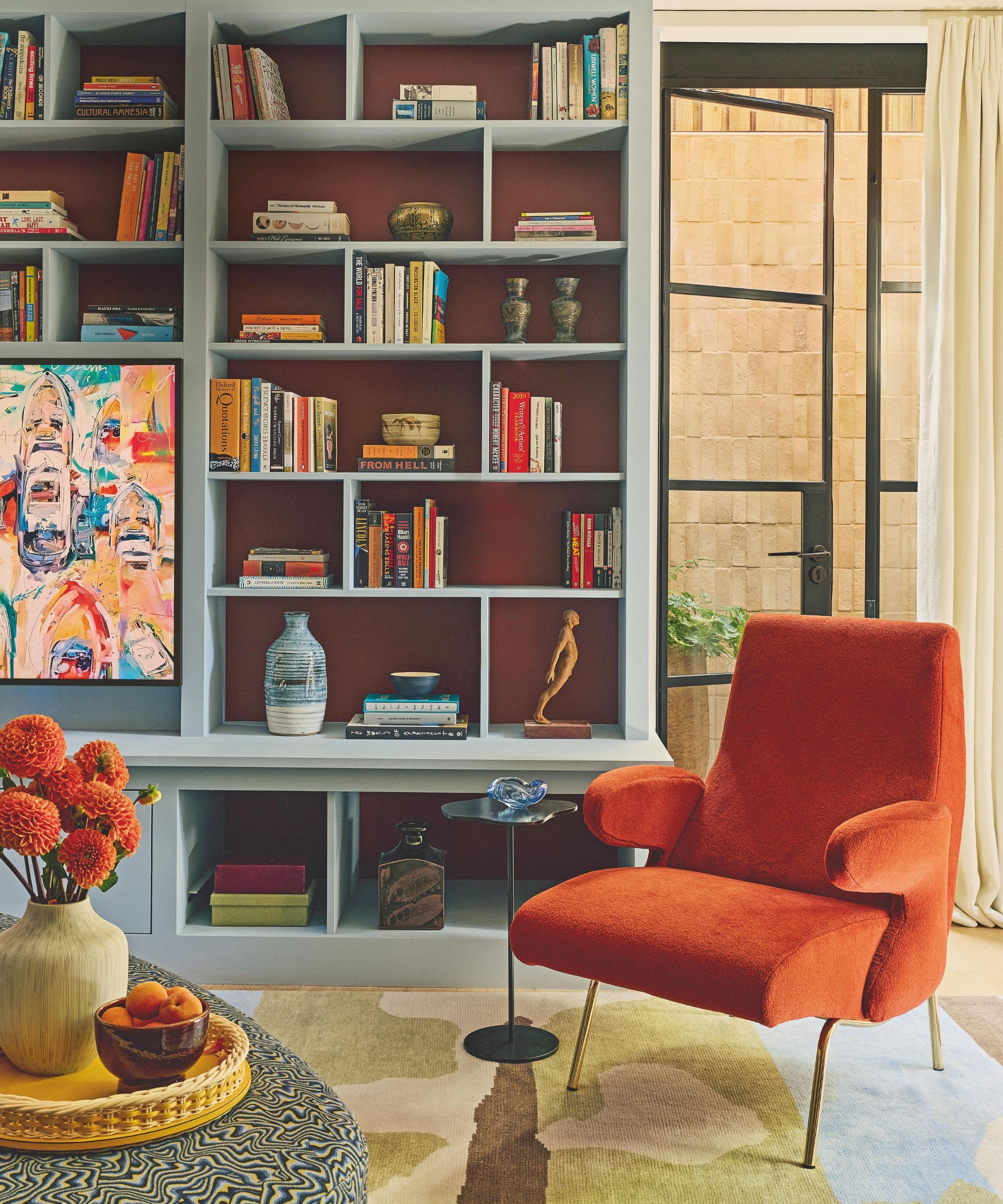 a family room in a london home with crittal doors out to the garden and a blue painted media wall styled with a geometric rug and orange armchair