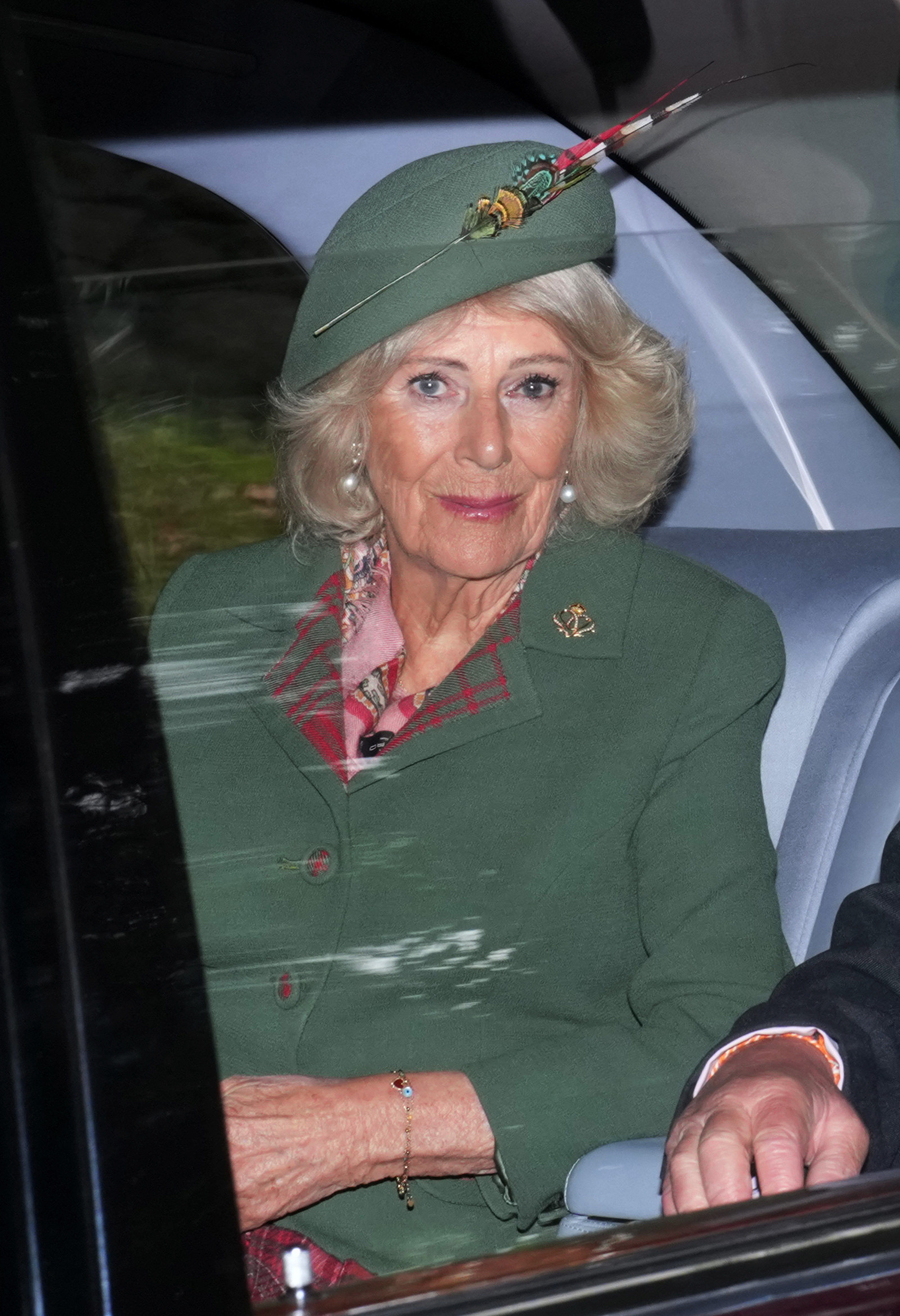 Queen Camilla wearing a green coat riding in a car