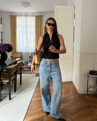 Anne wears a black halter top, blue baggy jeans, black mules, a straw bag and black sunglasses.