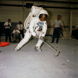 Photo of Neil Armstrong testing an Apollo spacesuit and moon rock gathering techniques