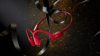 A pair of red Shokz headphones floating, with a black ribbon and gold dust nearby