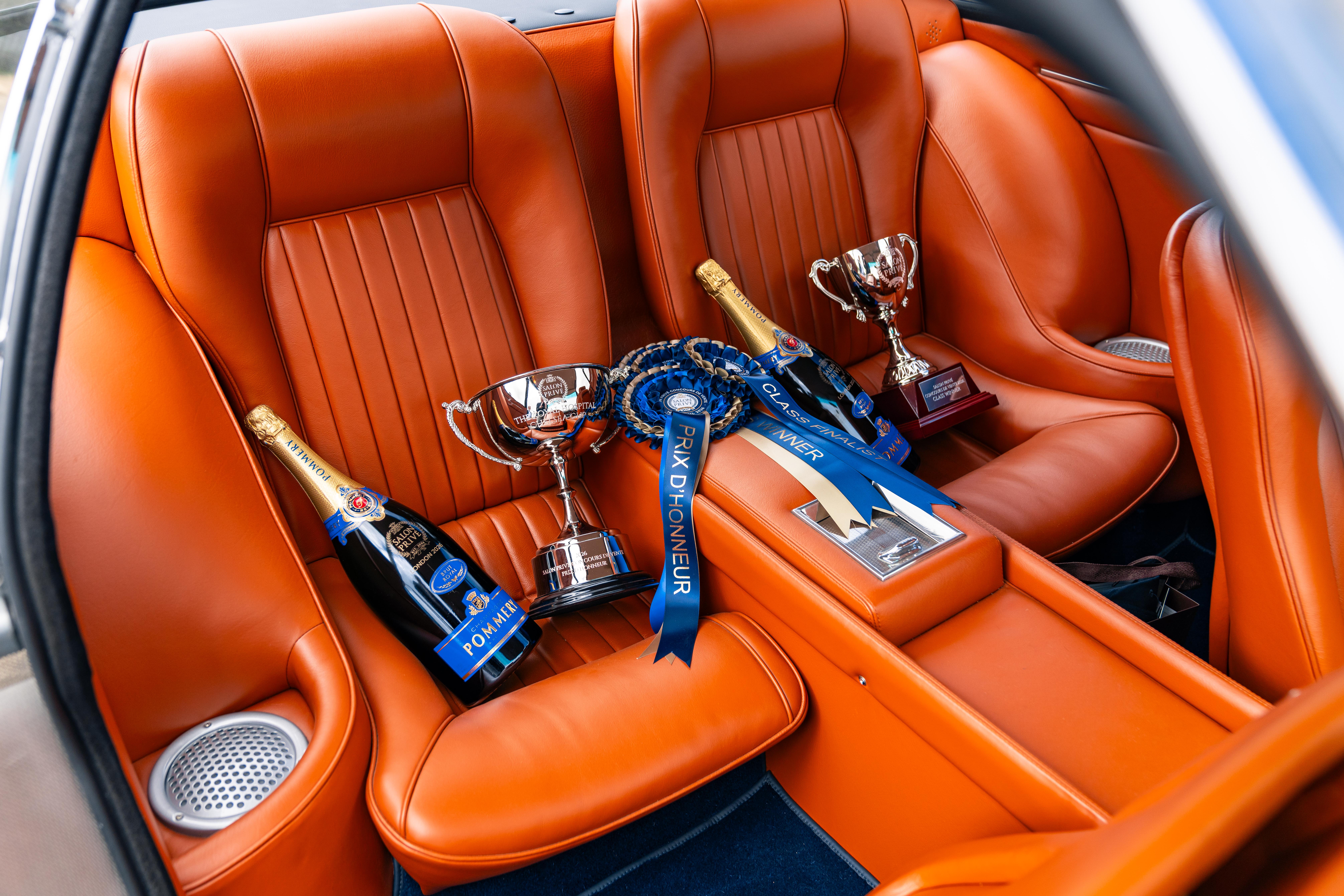 An array of trophies and medals in the back of a car with orange leather seats