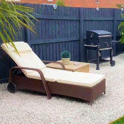 Lounger on gravel area next barbecue and blue wooden fence