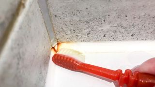 Cleaning grout in corner with toothbrush