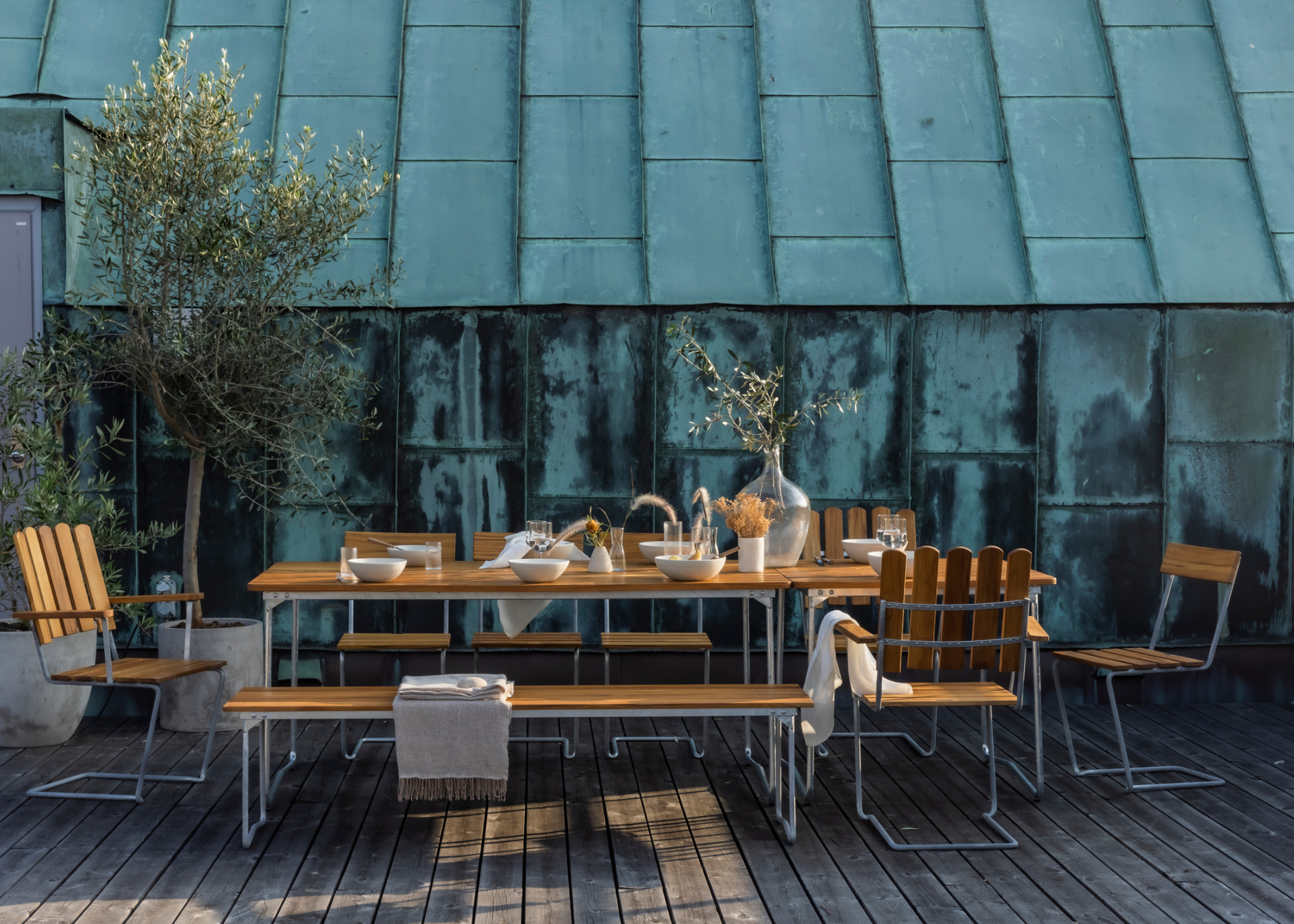 Grythyttan wood and metal dining set pictured on a wooden porch, outside of a rusted greenhouse