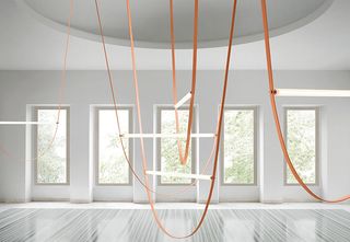 A large bright room with five tall windows and striped marble floor. An installation of Formafantasma's Wireline lights for Flos features several pink downward arches with tube light source