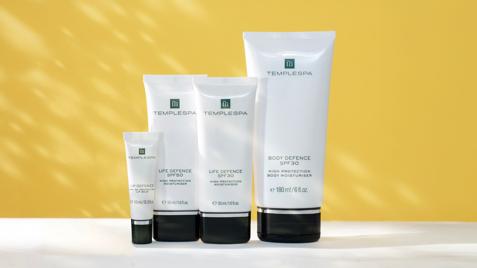 An image of TEMPLESPA SPF range including LIP DEFENCE, IIFE DEFENCE AND BODY DEFENCE on a yellow backdrop