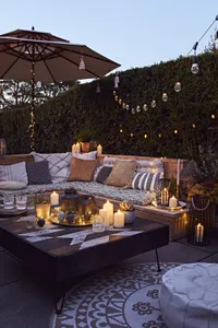 faux candles and fairy lights in an outdoor seating area with cushions and an aztec wooden bench