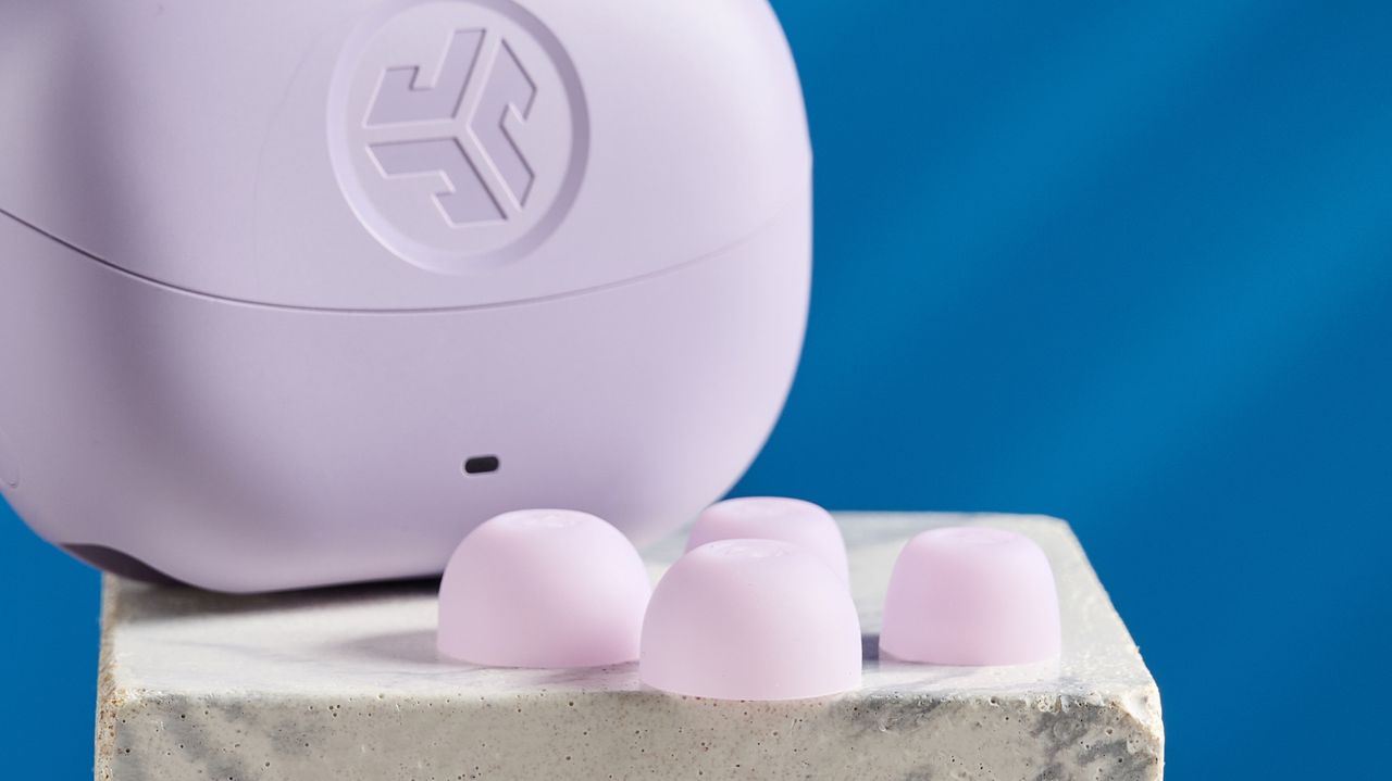 the jlab go pods anc earbuds in lilac with a lilac charging case and built in usb-c cable against a blue background on a marble stand
