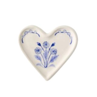 A white heart stoneware dish with a dark blue painted flower illustration on it