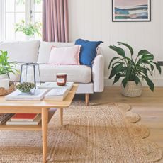 White living room with a white sofa, jute rug, and a wooden coffee table on top of it