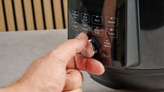 a black instant pot with a dial and touchpad is photographed against a blue background