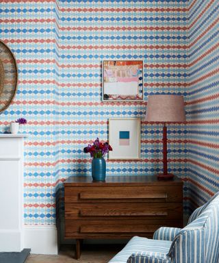 Dado's SAPOWAYDIDI patterned wall paper in blue on the walls of a small living room, a dark brown wooden drawer unit with a small lamp
