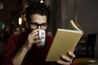 A man drinking a coffee while reading a book.