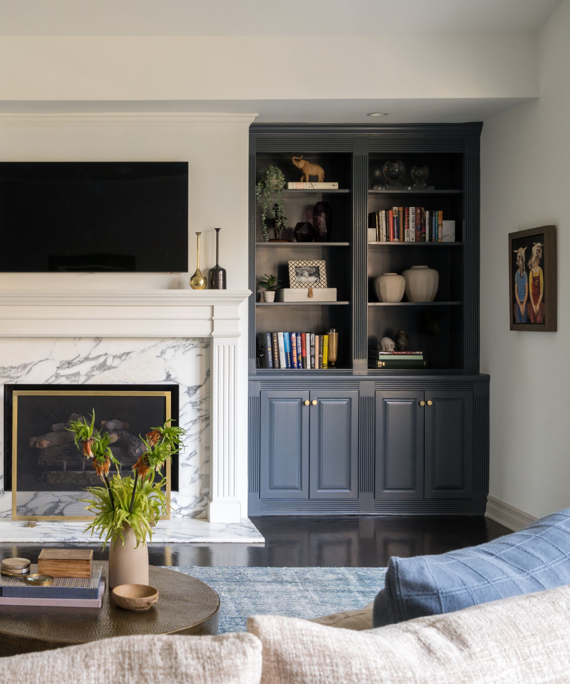 A living room with a white marble fireplace and dark blue bookshelves