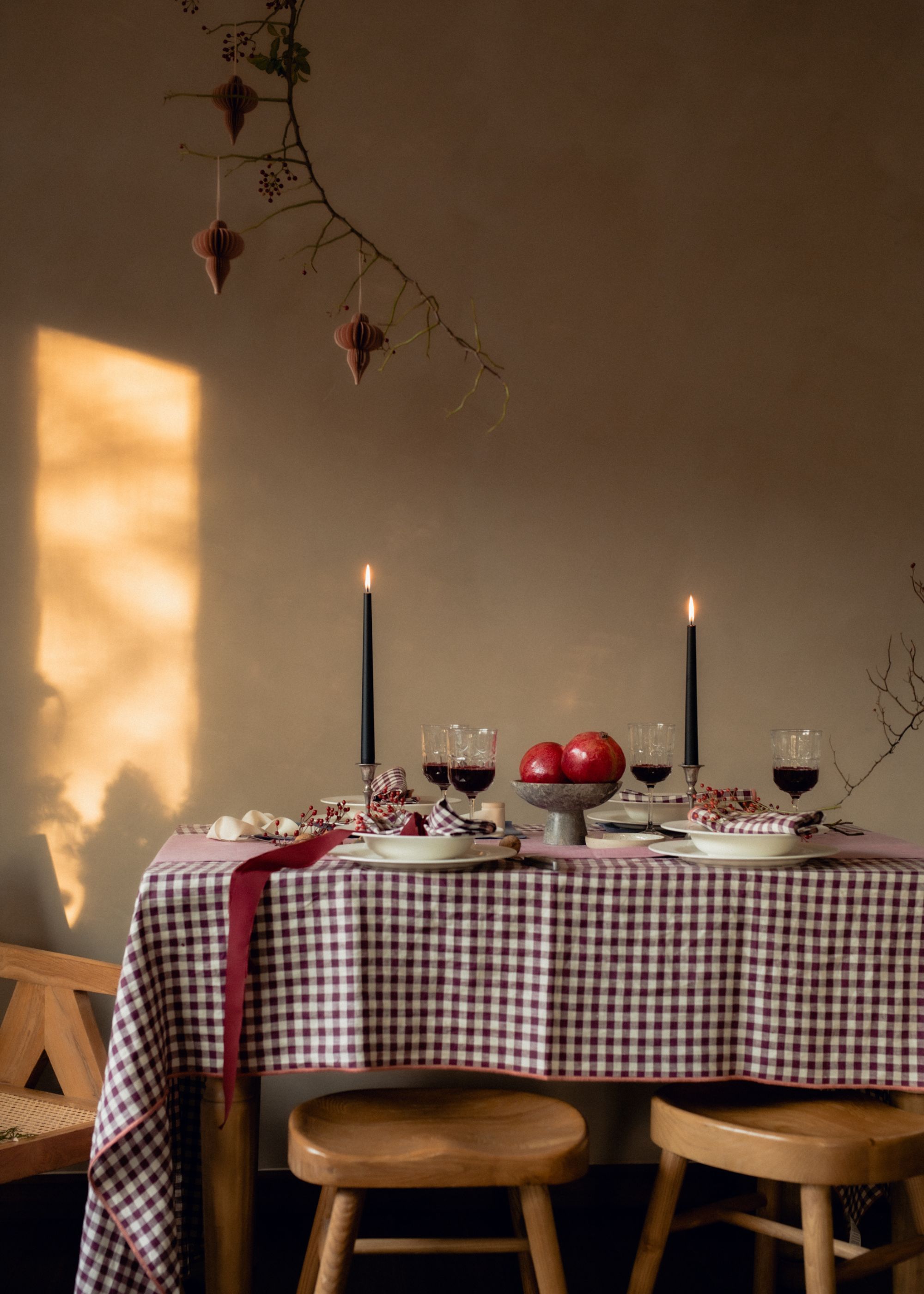 A dining table with a brown gingham tablecloth, two taper candles and seasonal decor.