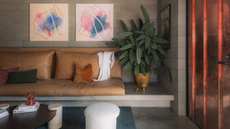 A leather sofa with abstract art on the wall and green foliage beside it 