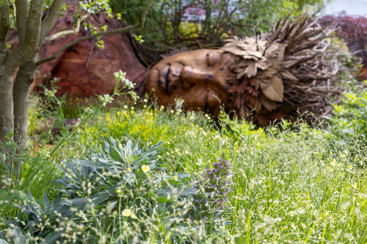 Images of the CPRE Show Garden On the Edge by Sarah Eberle. it focuses on grasses and flowers that grow around britain's edges, and is centred around a giant wooden carving of Gaia