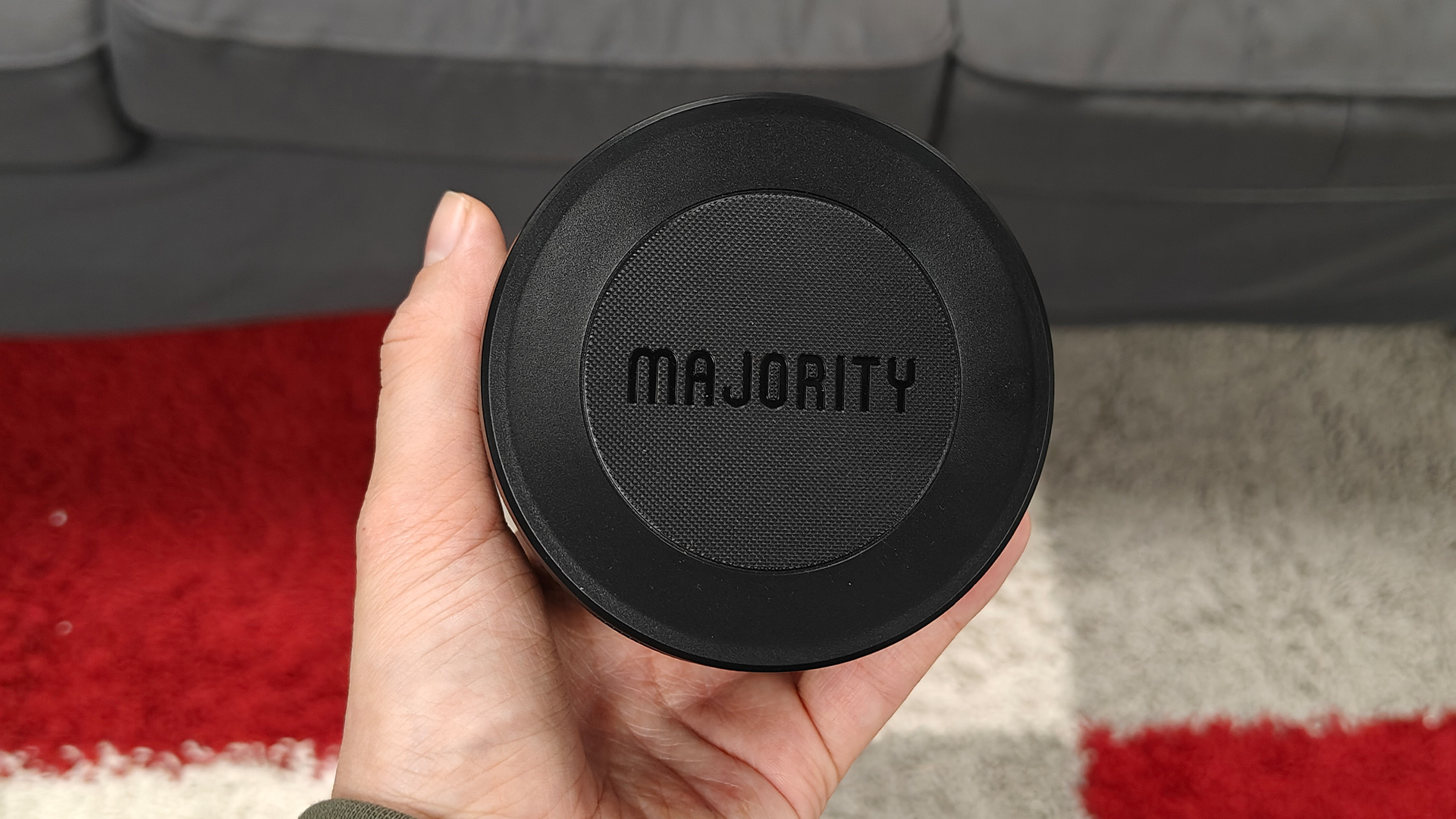 Majority Bowfell Halo Atmos soundbar system surround speaker held in hand above red white and grey rug