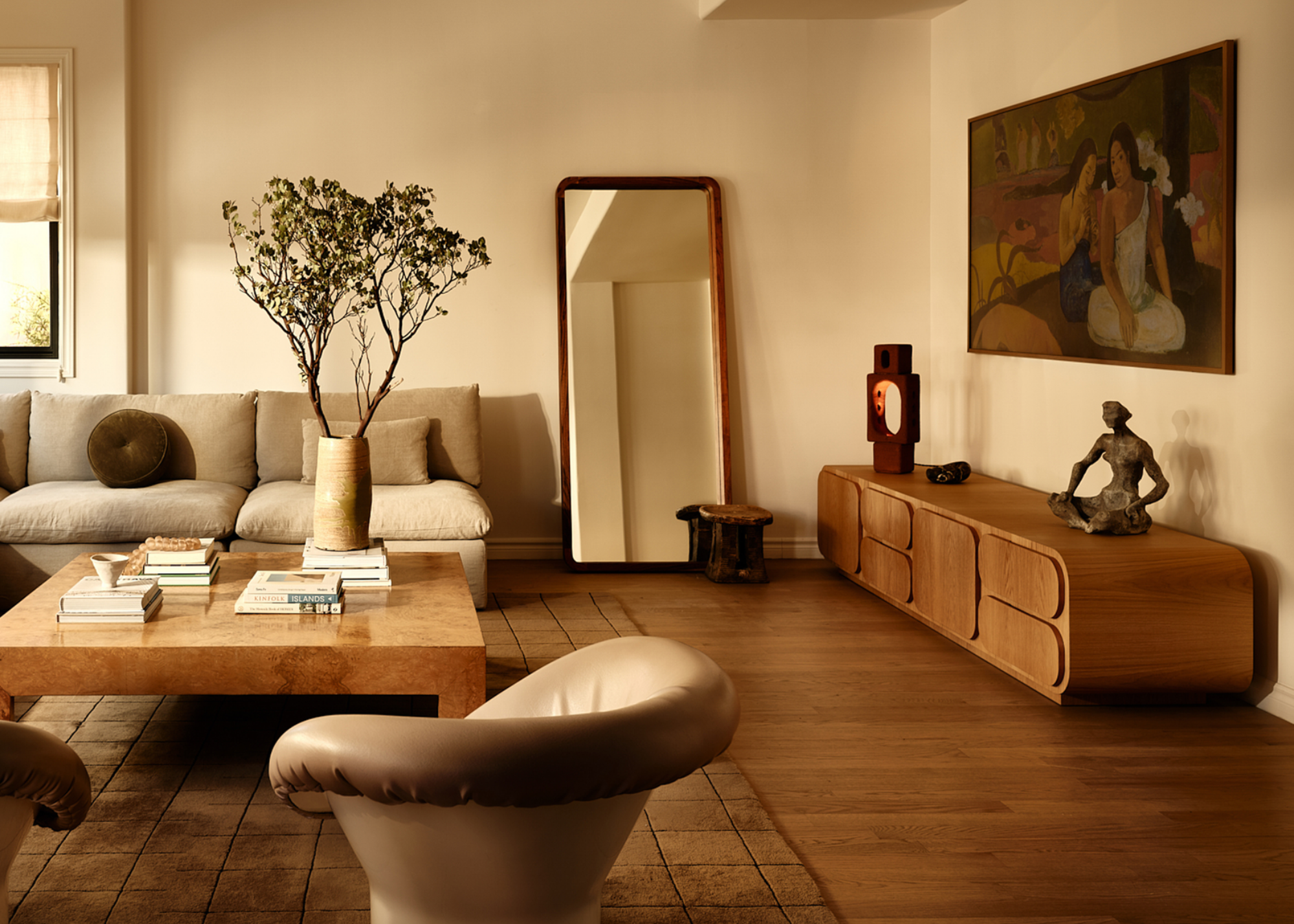 a beige living room with beige furniture, a mirror leant against the wall and a large cut branch in a vase on the coffee table