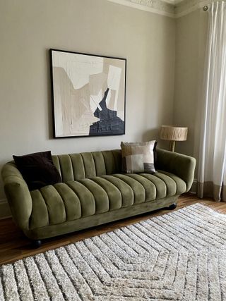 A living room with a green velvet sofa and artwork on the wall