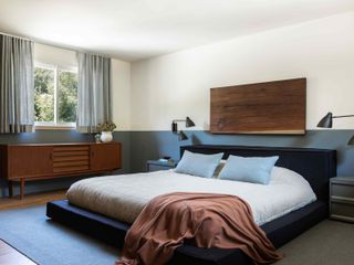 The bedroom of the house, with white and dusty blue walls and a wooden panel on the wall above the bed