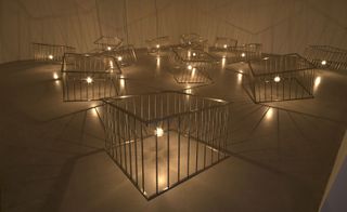 13 suspended metal playpen-like forms, each enclosing a hanging light