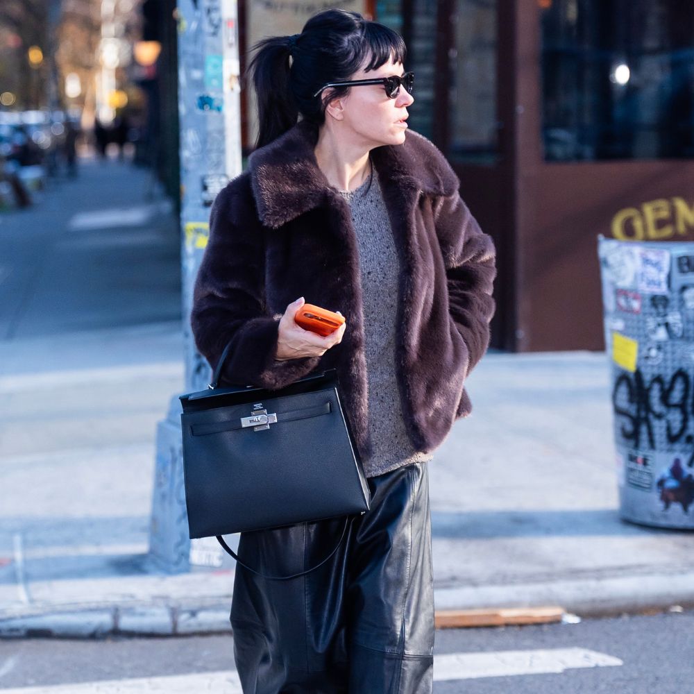 Lily Allen wears Hush fur jacket with a grey jumper a black leather skirt black lug-sole boots and a black Hermes bag and black sunglasses.