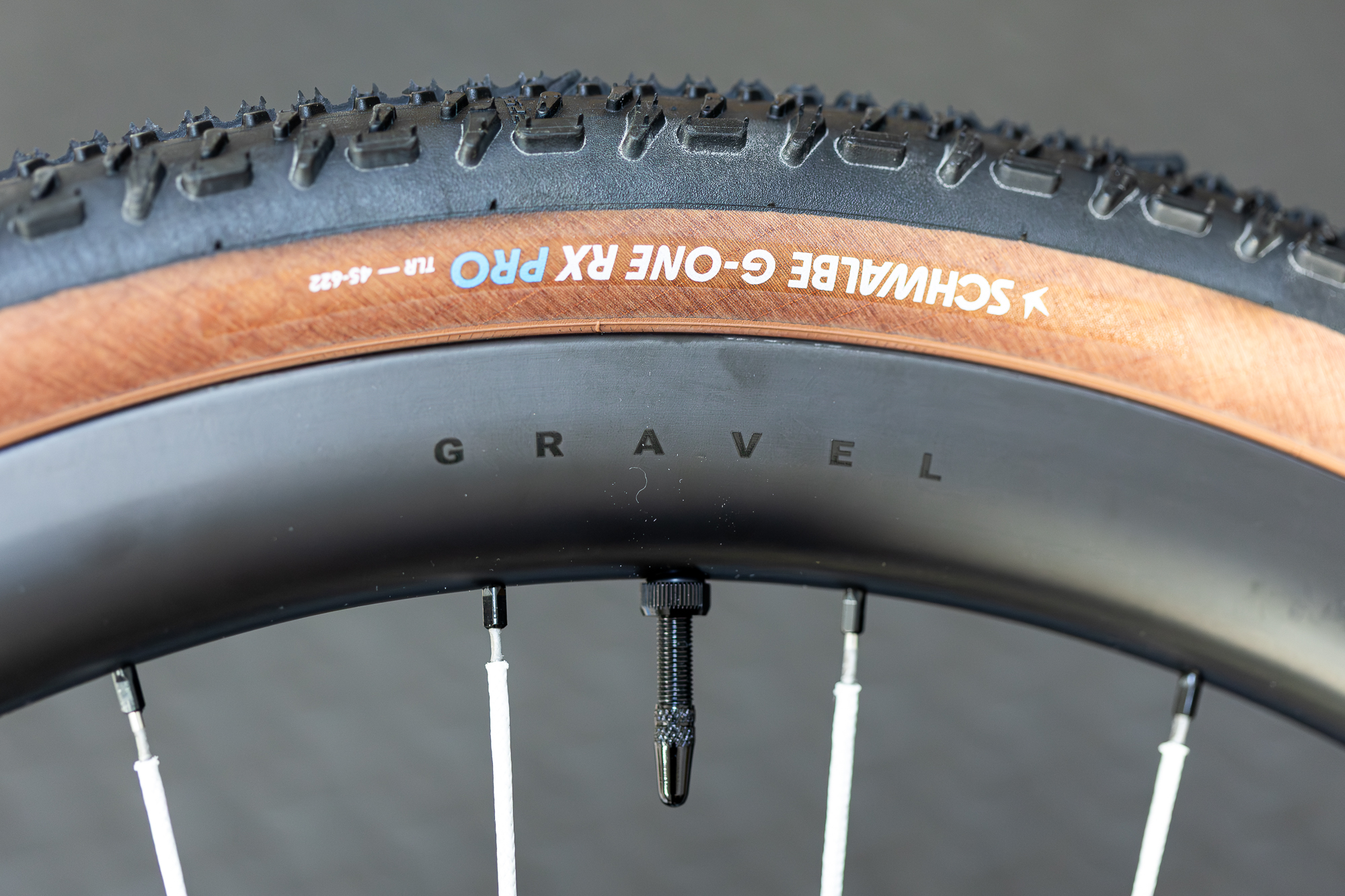 close up of a carbon rim with the word Gravel written on it and laced with white spokes, fitted with a tan wall Schwalbe gravel tyre