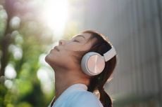 Headshot of young Asian woman with eyes closed, listening to music with wireless headphones