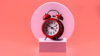 Red alarm clock on light pink box, in front of red and pink background